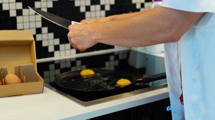 Camera moving back from young woman breaking eggs in cooking pan preparing breakfast in kitchen. Caucasian beautiful housewife in sexy red lingerie and white robe preparing food in modern home