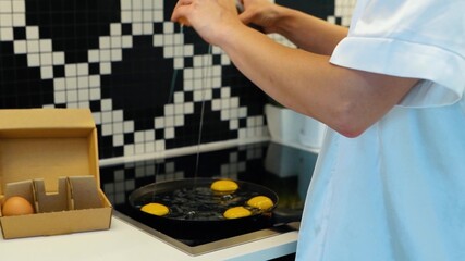 Caucasian positive young attractive woman frying eggs in cooking pan at home. Sexy beautiful lady in lingerie and white robe preparing breakfast in the kitchen. Food preparation. Slow motion