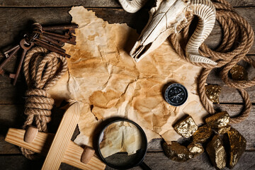 Skull of sheep with travel equipment, treasure map and golden nuggets on brown wooden background © Pixel-Shot