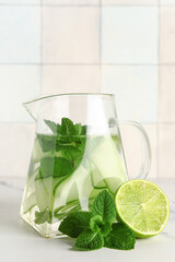 Jug of infused water with cucumber slices on white table