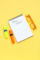 Notebook with empty to do list, markers and eyeglasses on yellow background. New year goals