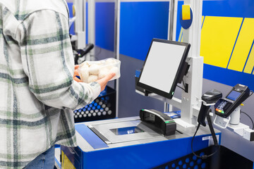 A customer holds mushrooms at a self-checkout counter in a supermarket
