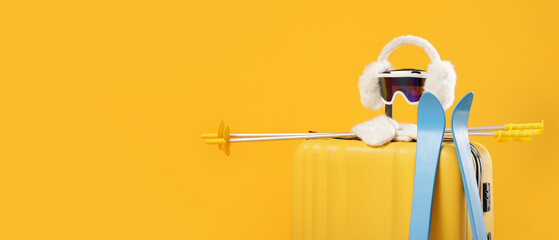 Suitcase with winter accessories and skis on yellow background