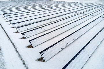 Aerial view of sustainable electrical power plant with solar photovoltaic panels covered with snow in winter for producing clean energy. Concept of low effectivity of renewable electricity in north