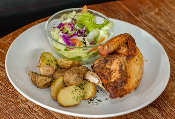 Roasted chicken served with baked potatoes and fresh vegetable salad on white plate. Restaurant style comfort food ideal for menu design, food advertising, healthy dinner, and casual dining concept