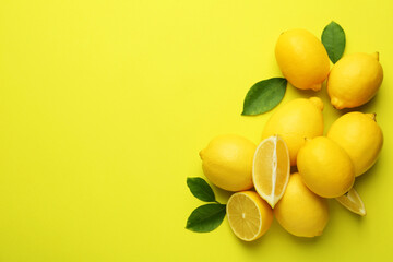 Fresh ripe lemons and leaves on yellow background, flat lay. Space for text