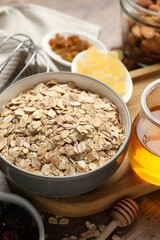 Making granola. Oat flakes in bowl, dried fruits and honey on wooden table, closeup