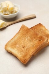Slices of toasted bread and butter on beige table, closeup