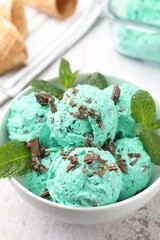 Tasty mint chocolate chip ice cream with leaves and waffle cones on light table, closeup