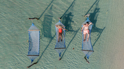 Relaxation takes center stage as two people lounge in colorful hammocks over the crystal-clear waters of Koh Kood Island, Thailand, surrounded by the serene beauty of nature on a sunny day.