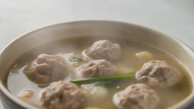 Bakso meatballs served in a savory broth with green onions in a dark bowl on a light background viewed from above