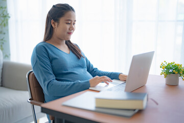 Pregnant asian woman using laptop at home pregnant businesswoman typing on laptop working on remote project in home office pregnancy concept