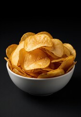 Potato chips in white ceramic bowl on black background. Snack food and fast food concept for packaging, advertisement with copy space
