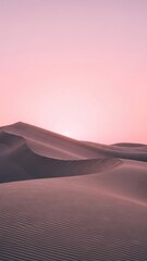 Soft pink sky over vast desert sand dunes at sunrise, creating a serene and minimalist landscape.