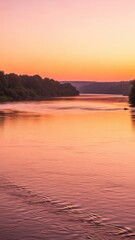 A serene river flows gently at sunset, reflecting the vibrant orange and pink hues of the sky, with lush green trees lining the distant banks.