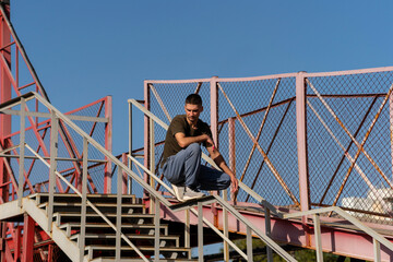 Freerunner pauses in balanced squat on stair handrail within a metal parkour zone, showing calm and control in urban training under clear daylight