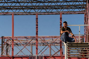 Urban athlete maintains stable position on handrail, showcasing focus and body awareness while seated on a high stair section of a red steel parkour structure