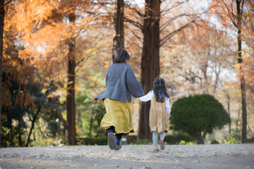 Fototapeta premium 秋の公園で一緒に娘と手を繋ぐちょっと高齢のママさん 顔無しの後ろ姿