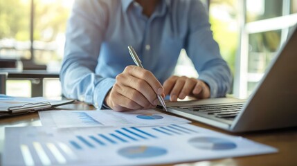 A man in a blue shirt working at a desk with a laptop and documents.