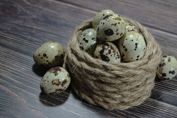 Obraz premium Fresh quail eggs arranged in a coiled jute rope nest on a dark wooden surface
