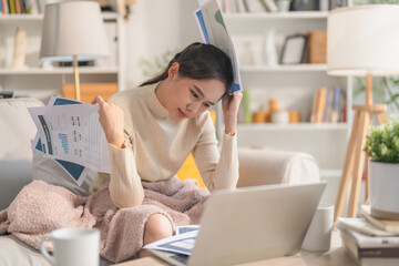 frustrated Asian woman is stressed at home with a laptop and paperwork, facing financial crisis or...
