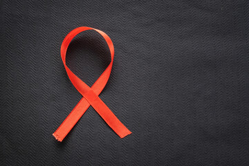 A vivid, red satin awareness ribbon is placed on a textured dark or black background, creating a strong, symbolic contrast. This image represents global solidarity and the fight against HIV AIDS.
