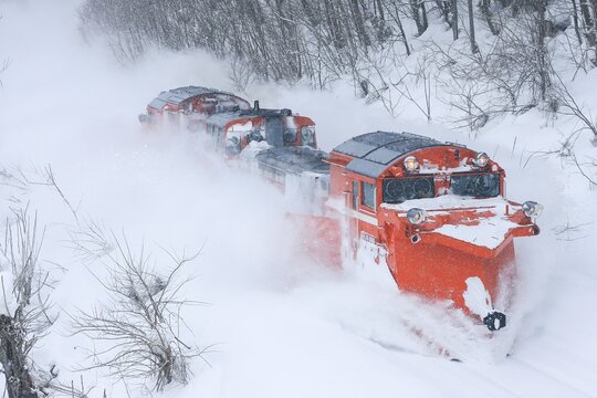 Red snowplow trains clearing railway tracks during heavy snowfall in rural Japan 