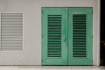 Industrial facade featuring green metal double doors and a white louvered ventilation window.