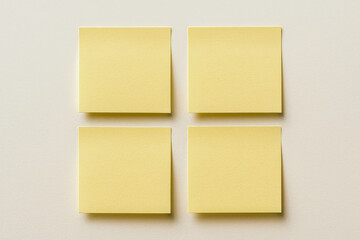 Fototapeta premium Horizontal photo of four yellow sticky notes arranged in a clean grid on a neutral background, bright and organized mood with soft shadows, minimal composition and clear structure, ideal for planning 