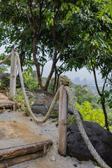 Rope barrier along a rustic path surrounded by trees and rocky ground on a hillside view