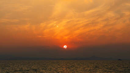 Sun Caught Behind Clouds Over the Sea Under an Orange Sky