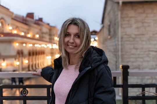 Woman portrait smiling in jacket near illuminated city street architecture at twilight - Powered by Adobe