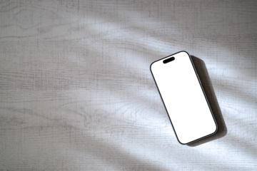 木漏れ日のある白木のテーブルの上にあるスマートフォン