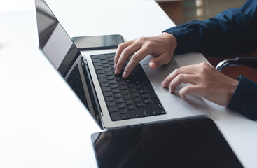 Business man working on laptop computer, typing on keyboard with digital tablet and mobile phone on white table at office. Man durfing the internet on portable computer