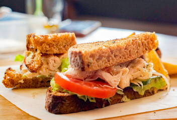 Close-up of a healthy homemade chicken sandwich with fresh lettuce and tomato on whole grain bread, served on parchment paper with blurred café background. Ideal for lunch, café, and clean eating