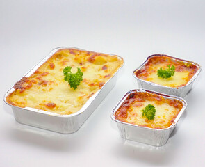 Freshly baked cheese lasagna served in aluminum foil containers. Comfort food concept for catering, takeaway meals, food delivery, or ready-to-eat homemade dishes on white background