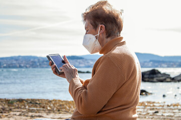senior woman in a medical mask uses a smartphone outdoors