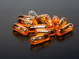 Close up of amber softgel capsules scattered on a gray surface, shot in studio lighting. Modern healthcare and nutrition concept showing vitamin, fish oil, or supplement pills for daily wellness