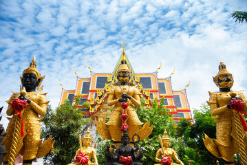 Group of large Thao Wessuwan (Giant Guardian) statues standing at a Buddhist shrine in Thailand under a cloudy blue sky. Golden and black giants holding clubs.