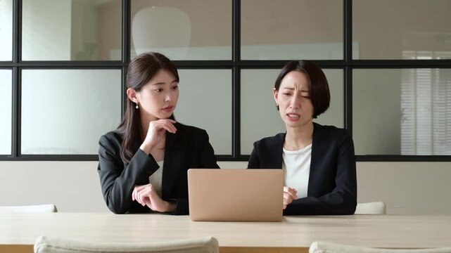 オフィスでパソコンを見て悩むスーツを着た2人の日本人女性