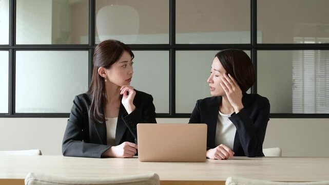 オフィスでパソコンを見て悩むスーツを着た2人の日本人女性