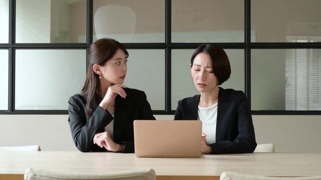 オフィスでパソコンを見て悩むスーツを着た2人の日本人女性