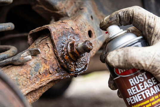 Spraying rust penetrant oil on suspended rusty bolt. Mechanic loosening stuck nu