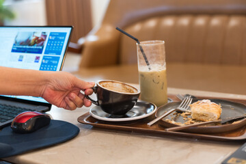 Close up business hand holding hot black coffee cup and ice coffee glass on wooden plate background.Delicious breakfast menu croissant and coffee cup on the wood table in the restaurant.