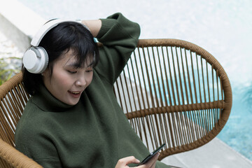Relaxed Asian woman leaning back on a wicker chair with headphones. Concept of stress relief,...