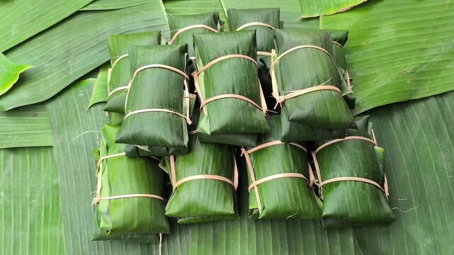Stacked Khao Tom Mud tied with string resting on fresh green banana leaves.