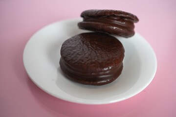 Two Chocolate-Coated Biscuits with Marshmallow Filling on a White Plate, Studio Shot on Pink Background.