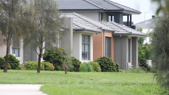 A row of modern detached houses or contemporary homes in Tarneit, Melbourne Australia features tiled roofs, overlooking public green space with grassy lawn and young trees. 