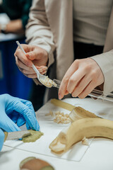 Close-up of hands placing diced banana into a test tube using a spoon, with banana peels and a...