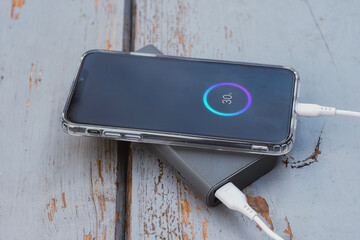 Smartphone connected to a portable power bank showing battery charging progress on the screen. Modern mobile technology concept with charging cable and digital battery indicator.